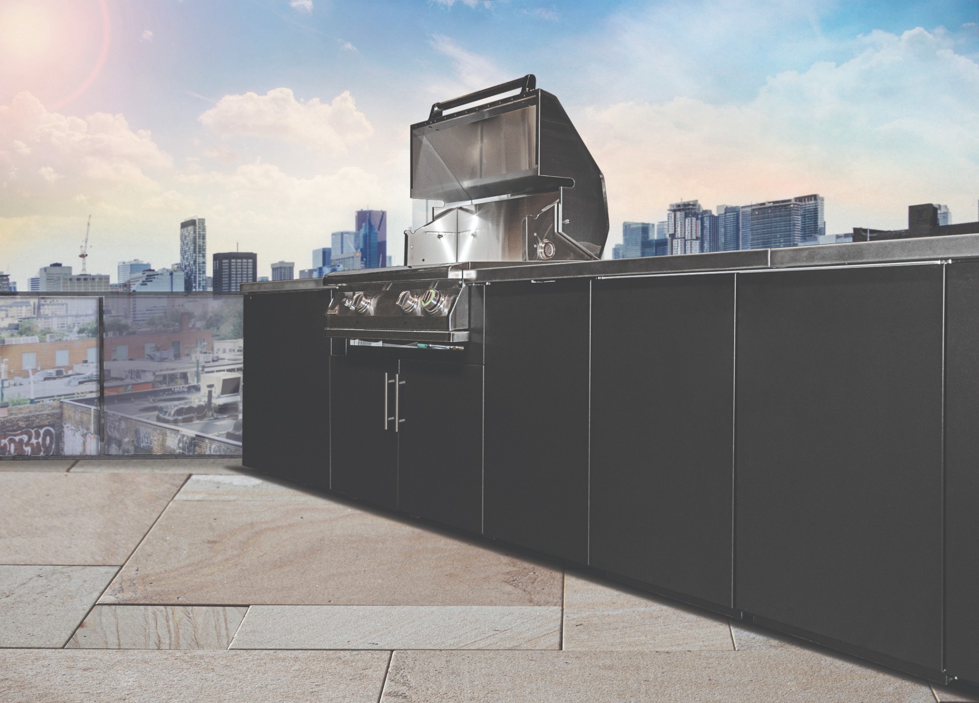 Black outdoor kitchen with a stainless grill on a stone-paved rooftop overlooking a city skyline