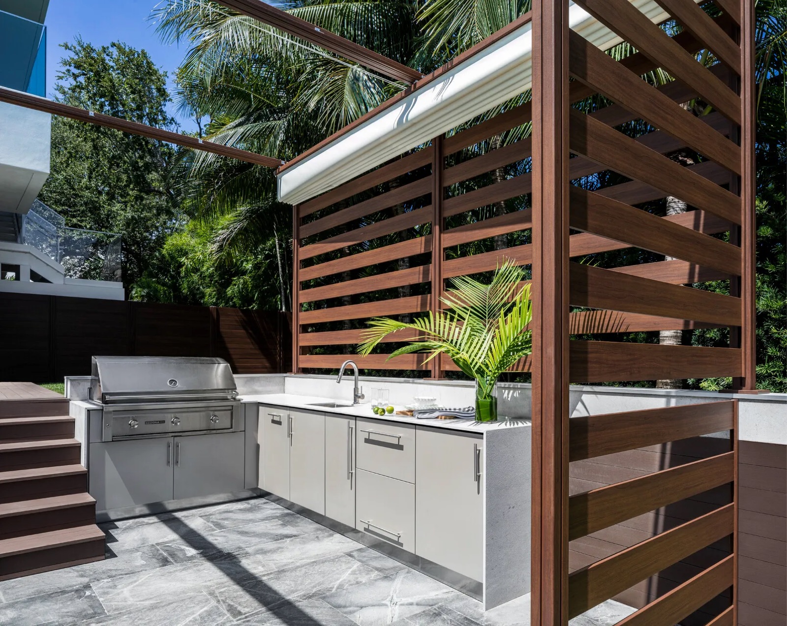 White outdoor cabinets and a stainless grill beside a slatted wood privacy screen