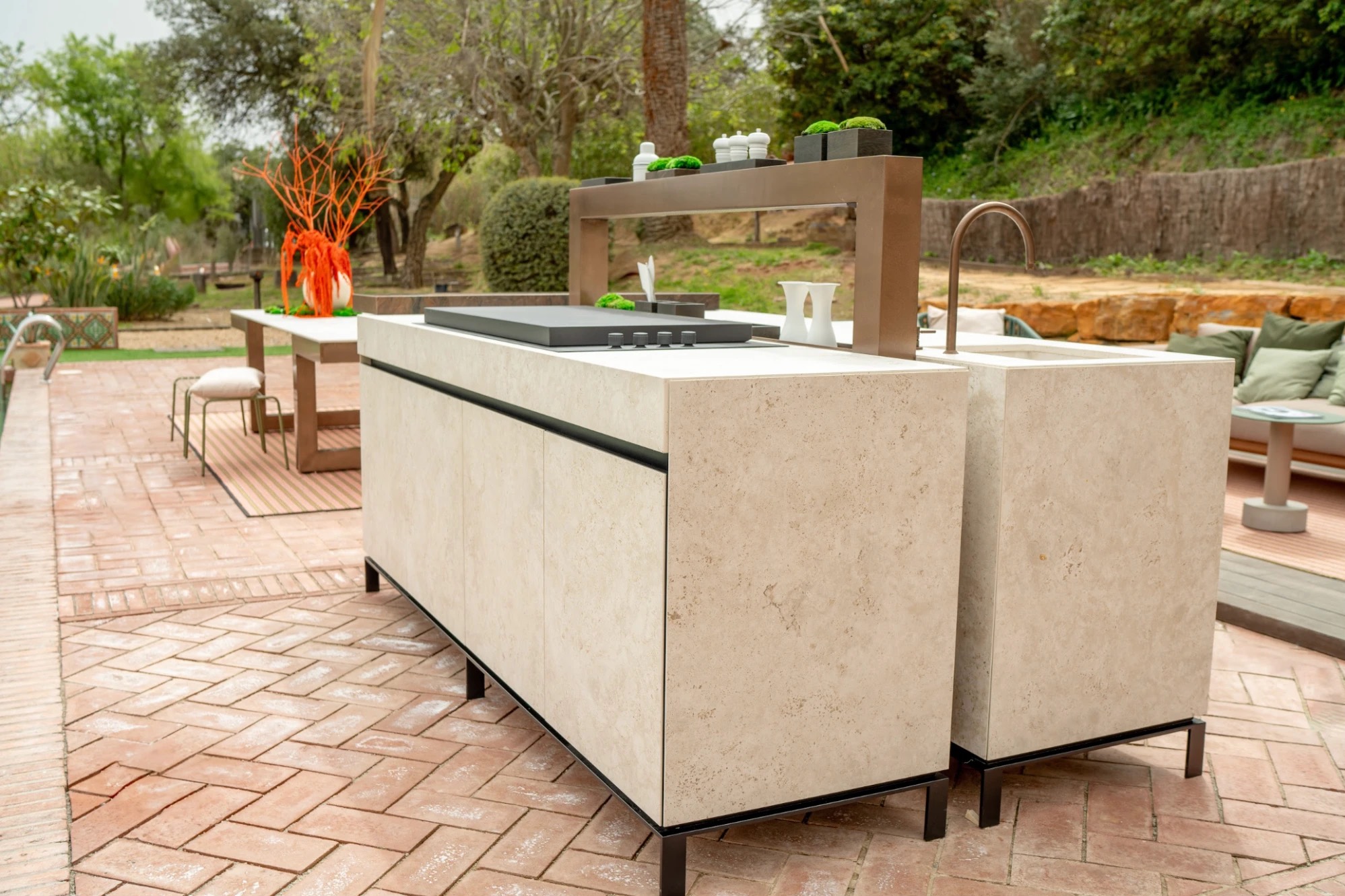 Travertine-look Novara island with a black cooktop and a bronze shelf frame on a brick pool terrace